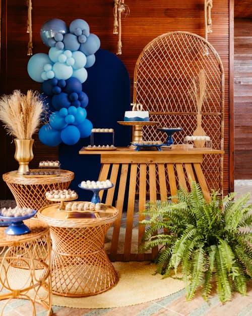 Mesa de doces com bolo e arco de balões azuis em festa de aniversário