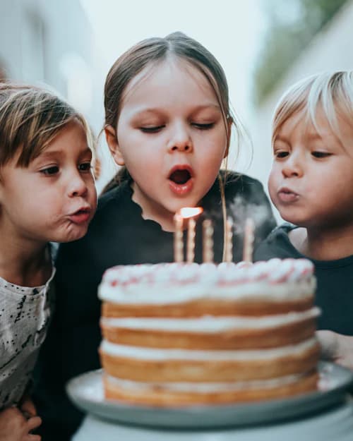 Três crianças em volta de um bolo, uma delas assoprando as velas