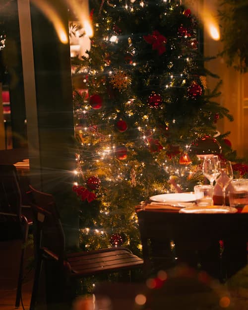 Árvore de Natal iluminada com a mesa da ceia posta ao fundo