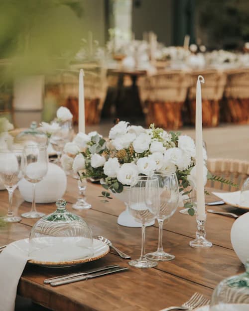 Mesa de casamento com arranjos de flores brancas, velas e taças