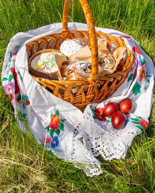 Cesta de Páscoa com pães e ovos pintados sobre toalha bordada na grama
