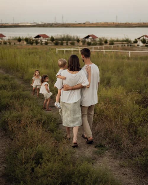 Família caminhando de costas por uma trilha de capim ao entardecer