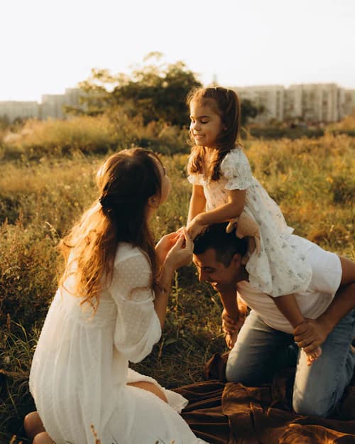 Mãe e crianças brincando em um campo aberto ao pôr do sol